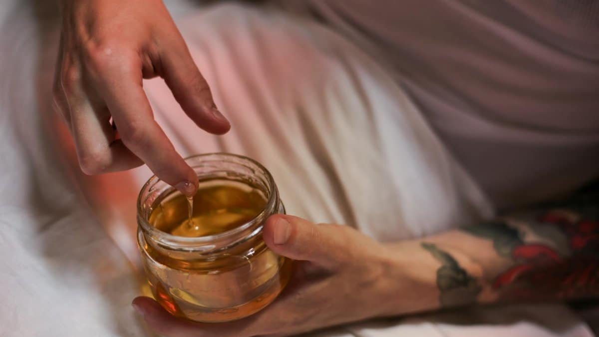 A tattooed person dips a finger into a honey jar, capturing a sweet and tactile moment.