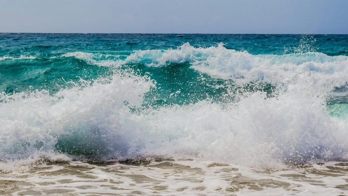 Dynamic ocean waves crashing onto a sandy shore under daylight, showcasing nature's power and beauty.