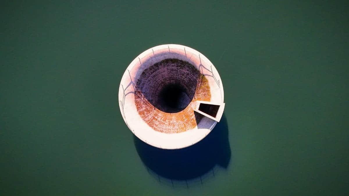 Aerial view of a bell mouth spillway in a calm reservoir, highlighting engineering and architecture.