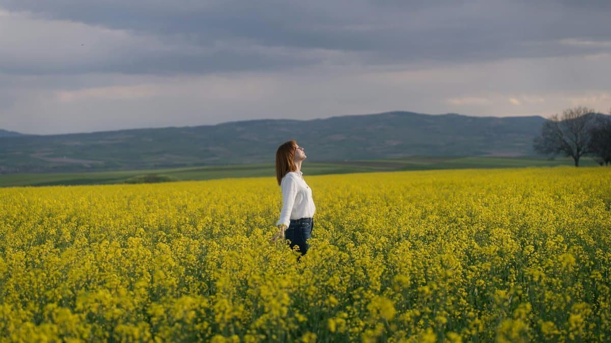 A woman enjoying tranquility in a vibrant yellow canola field under a cloudy sky in Merzifon, Türkiye.
