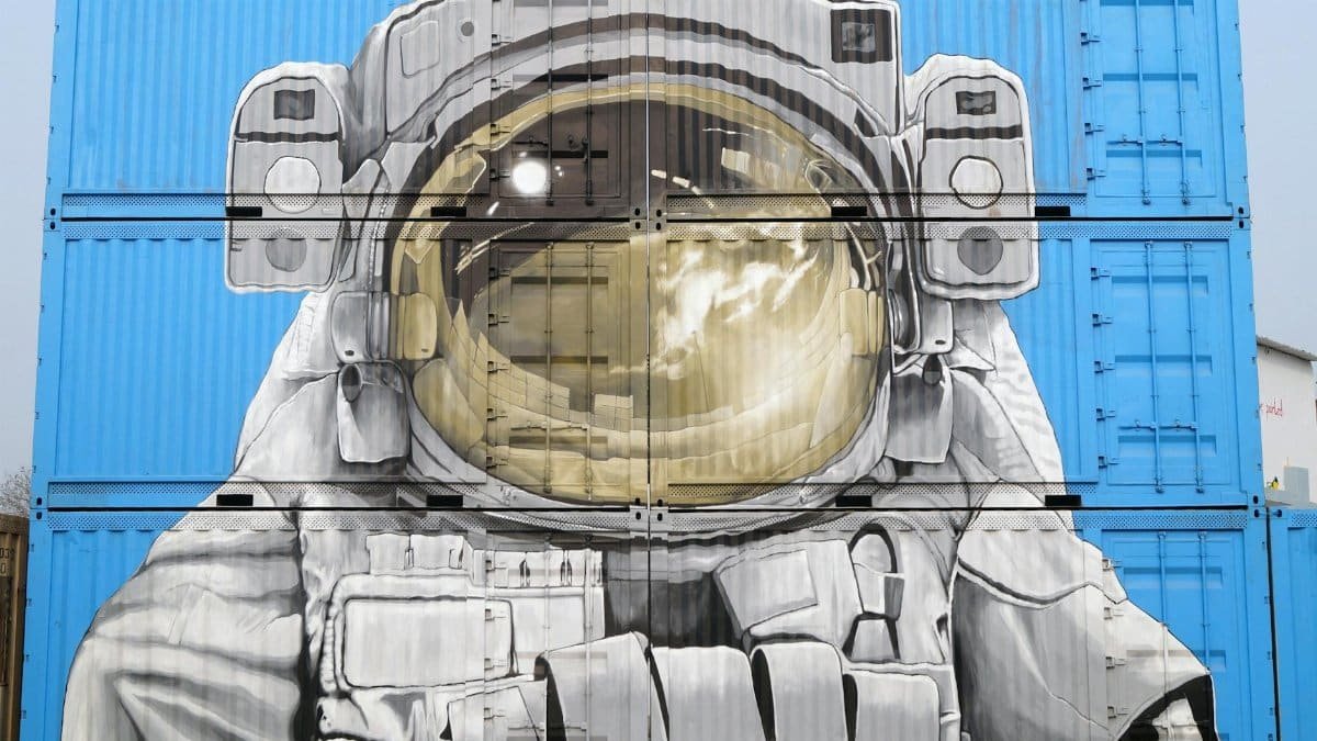 Astronaut mural painted on blue shipping containers, blending art and urban environment.