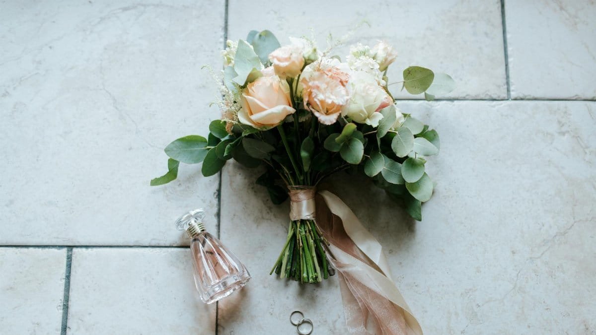 Beautiful wedding bouquet with roses, rings, and perfume bottle arranged on a tiled floor.