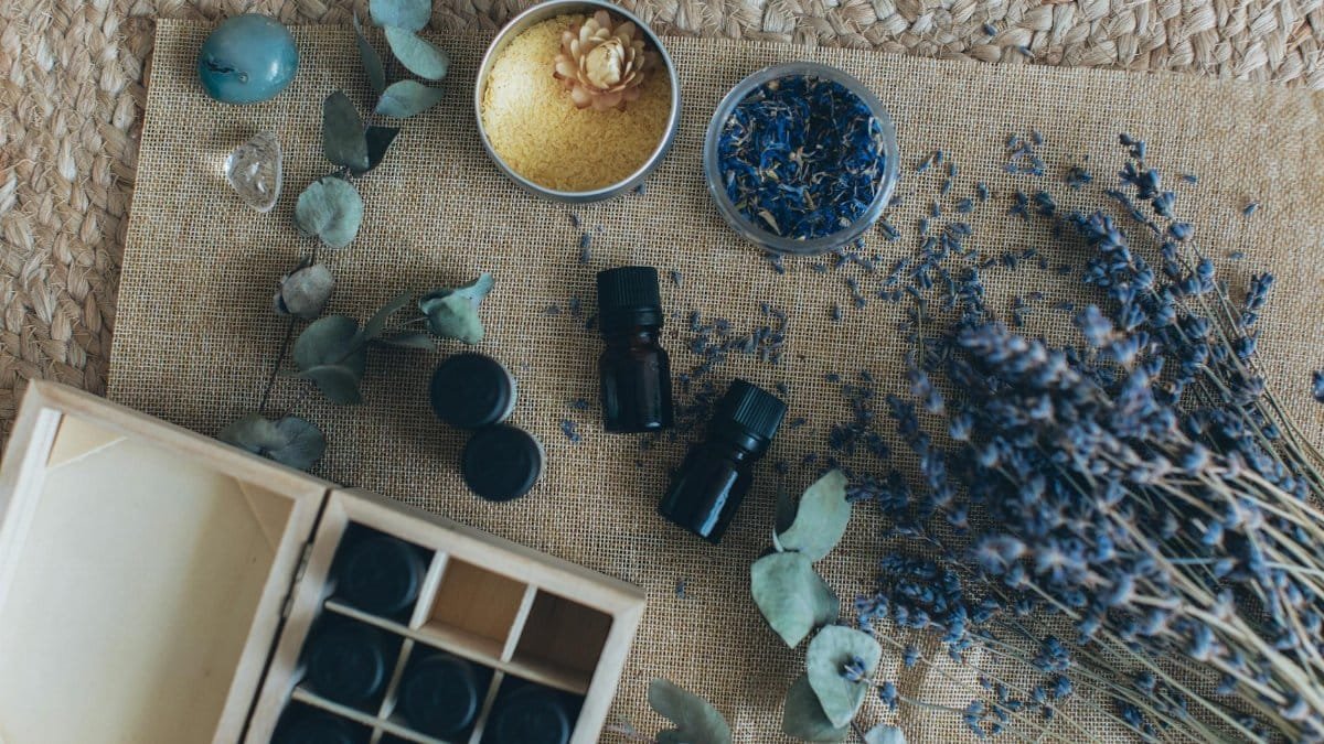 A flat lay displaying essential oils, dried lavender, and other aromatherapy items on a woven mat.