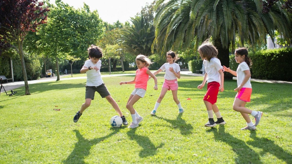 Group of kids enjoying a game of soccer in a lush green park on a sunny day in Portugal.