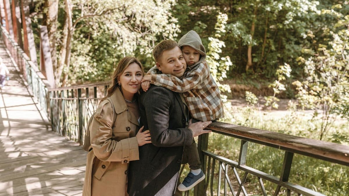 A family enjoying a sunny day outdoors, posing on a bridge surrounded by lush greenery.