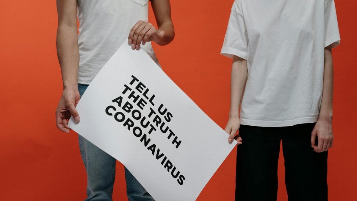 Two people holding a sign about coronavirus truth against an orange backdrop.