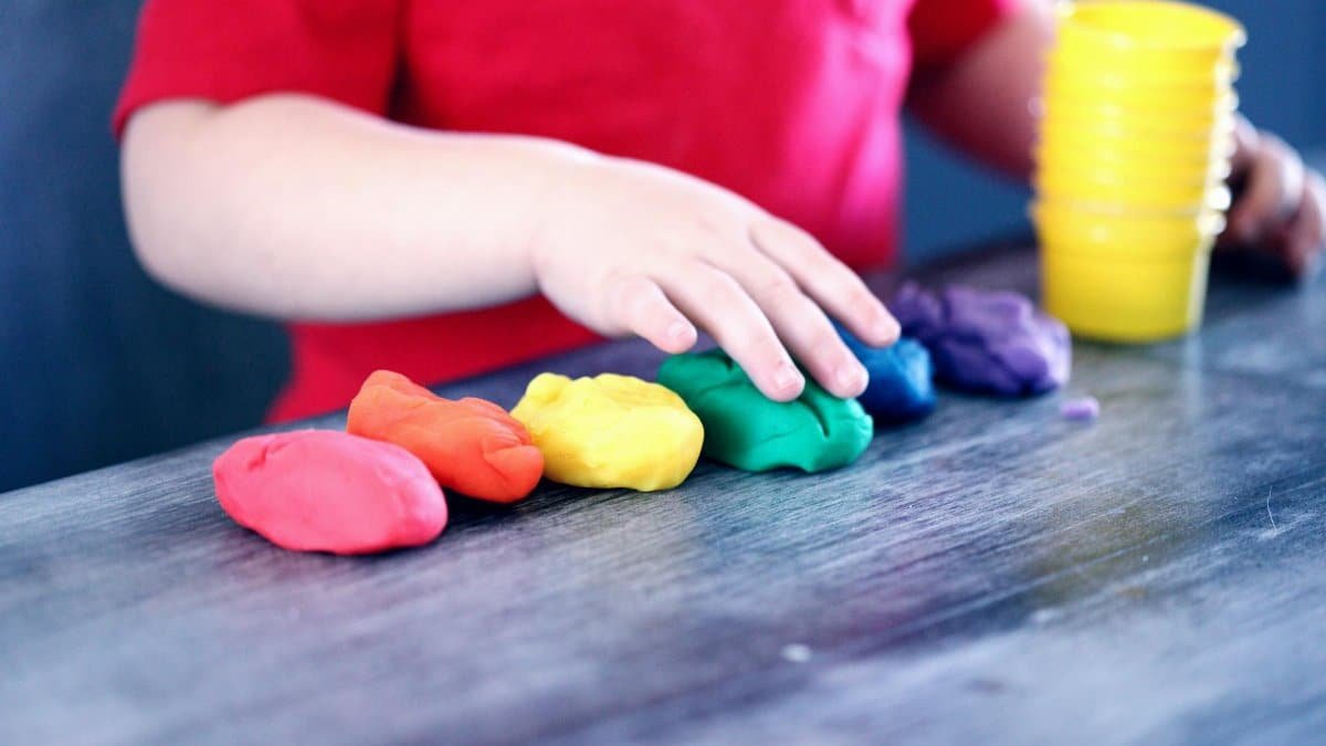 A young child with rainbow-colored modeling clay and stacking cups on a table indoors.