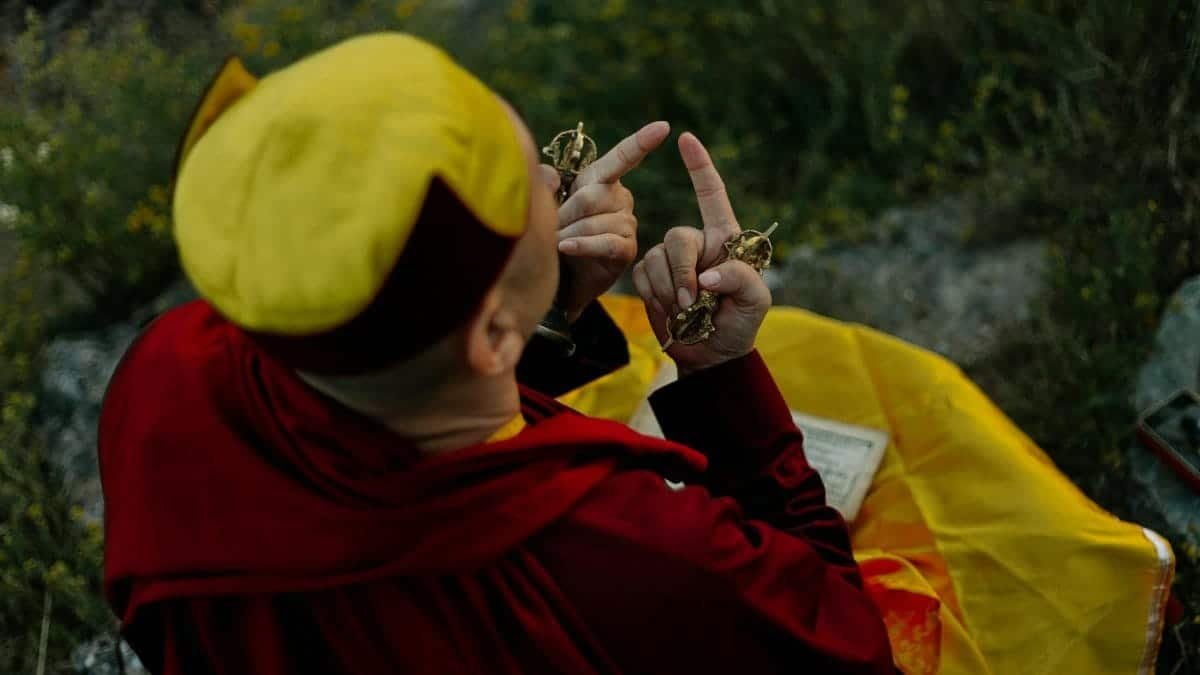 Tibetan monk meditating outdoors holding vajra and ghanta, symbolizing spiritual focus.