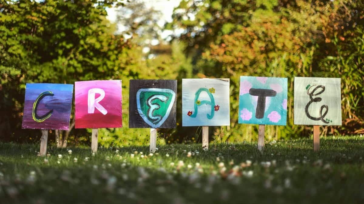 Vibrant painted signs spelling 'CREATE' in a lush outdoor garden setting.
