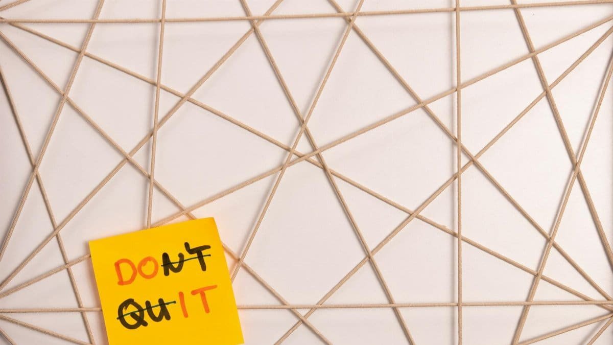 Bright yellow sticky note with motivational message on an abstract geometric design background.