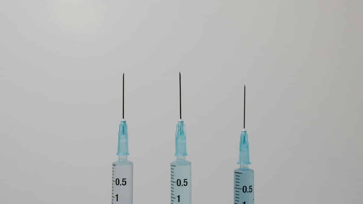 Close-up image of three syringes with needles against a neutral background.