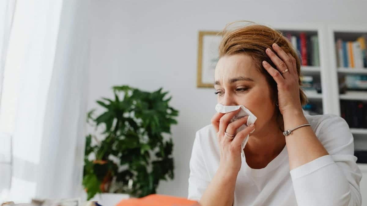 An adult woman feeling unwell, blowing her nose indoors.