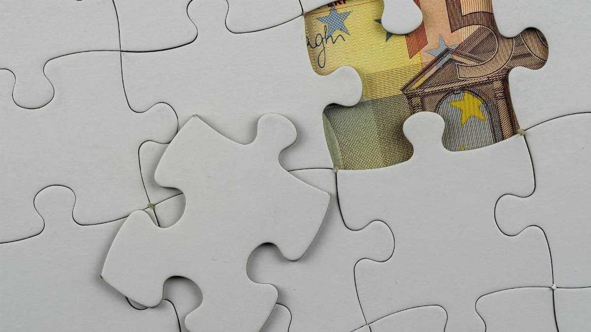 Close-up of a jigsaw puzzle missing piece revealing Euro currency underneath.