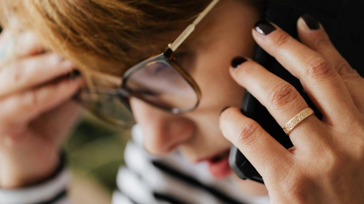 A woman wearing glasses and a ring, talking on a smartphone with a concerned expression.