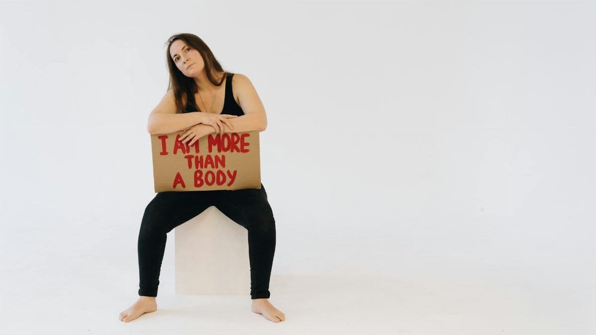 Woman holding 'I am more than a body' sign, promoting empowerment and equality.