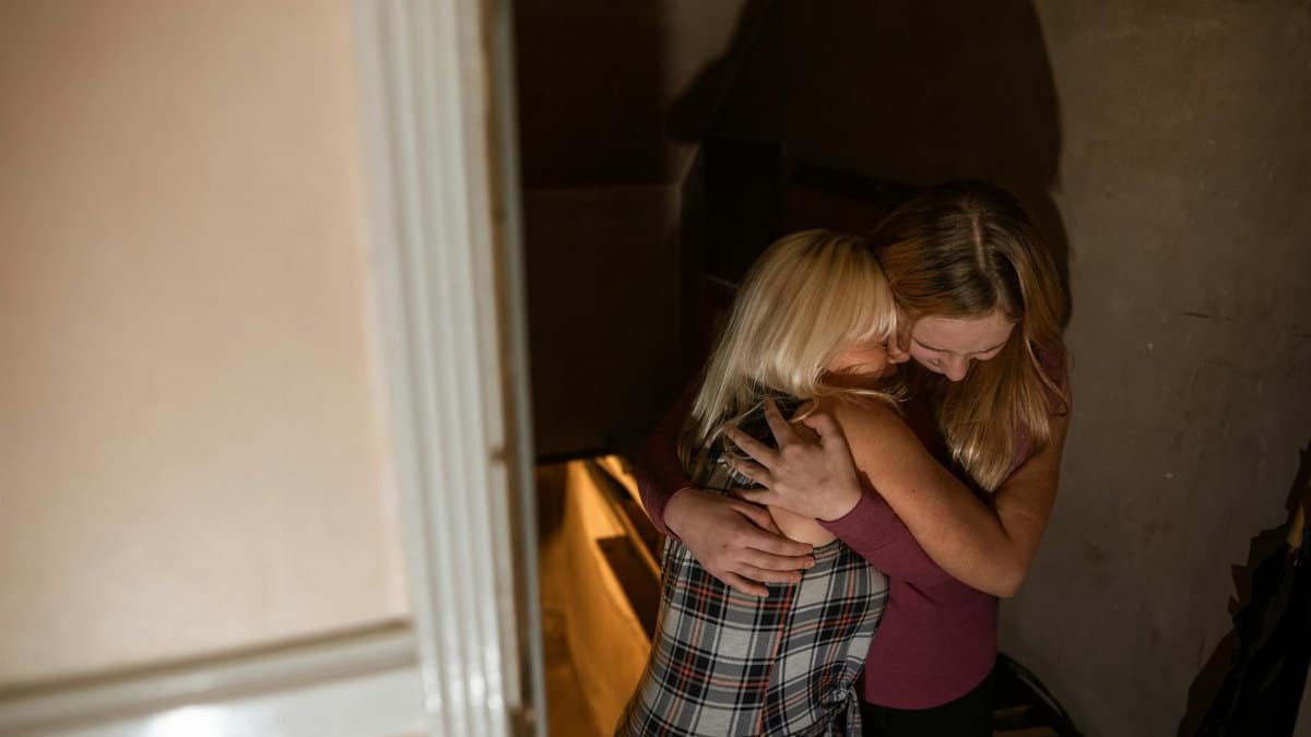 Two women embrace in a heartfelt hug, conveying warmth and support in a dimly lit room.