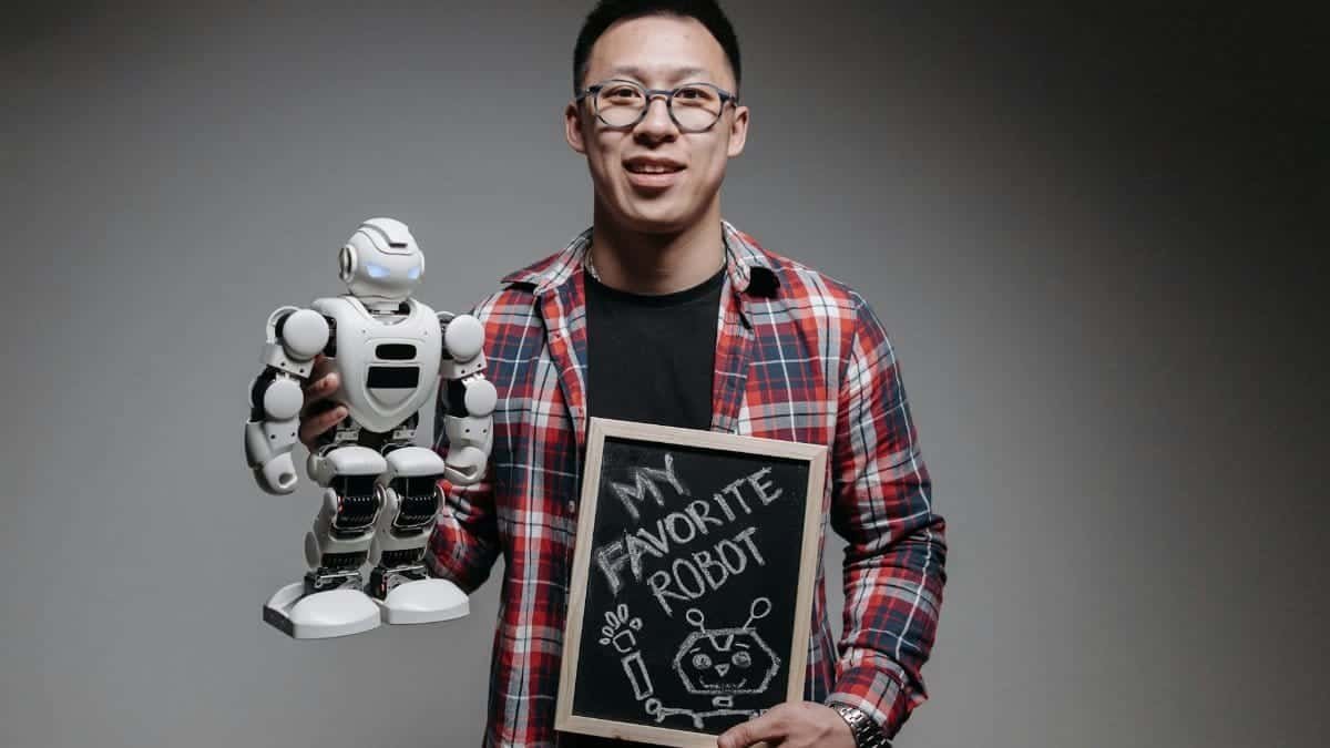 Smiling young man in plaid shirt holding a robot and chalkboard with text 'My Favorite Robot'.