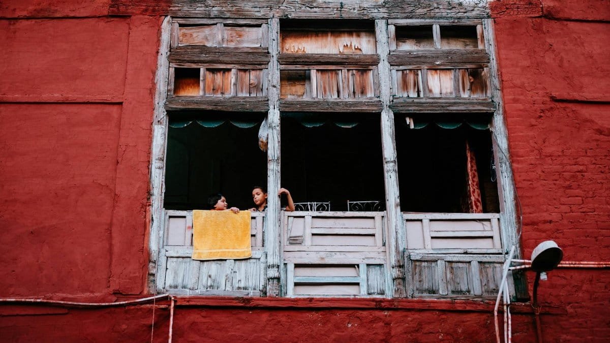 Children looking out of a rustic window with colorful walls in Lahore, capturing daily life.