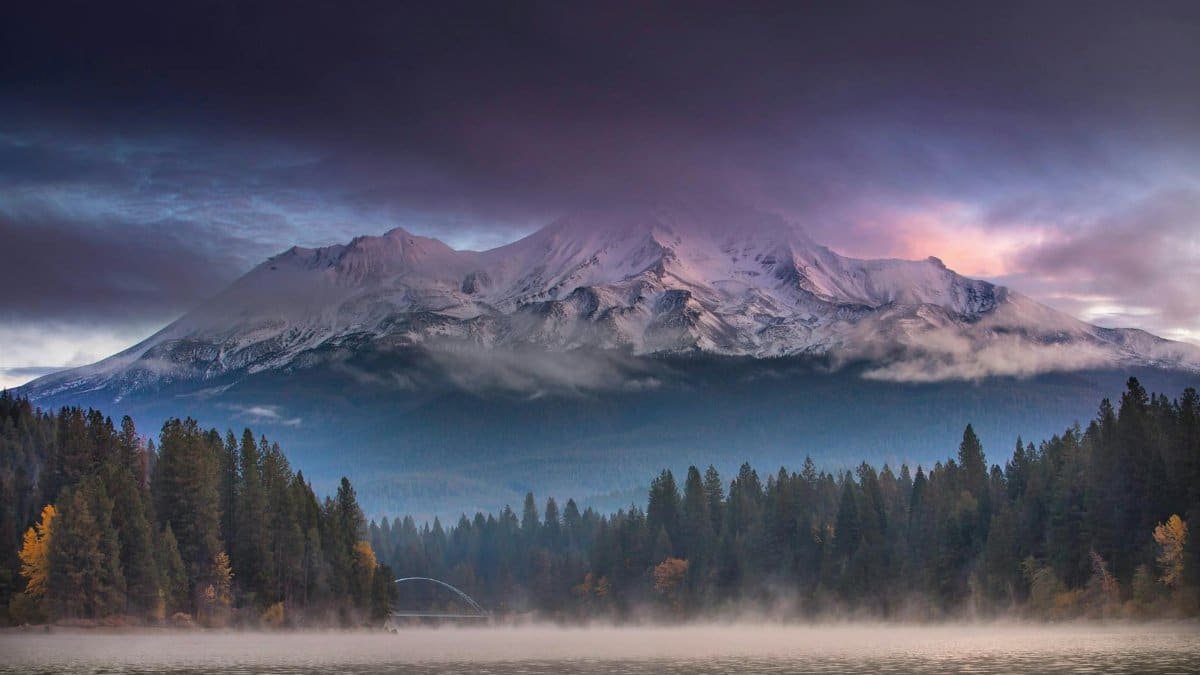 Captivating view of Mount Shasta with a misty forest foreground and dramatic clouds at twilight.