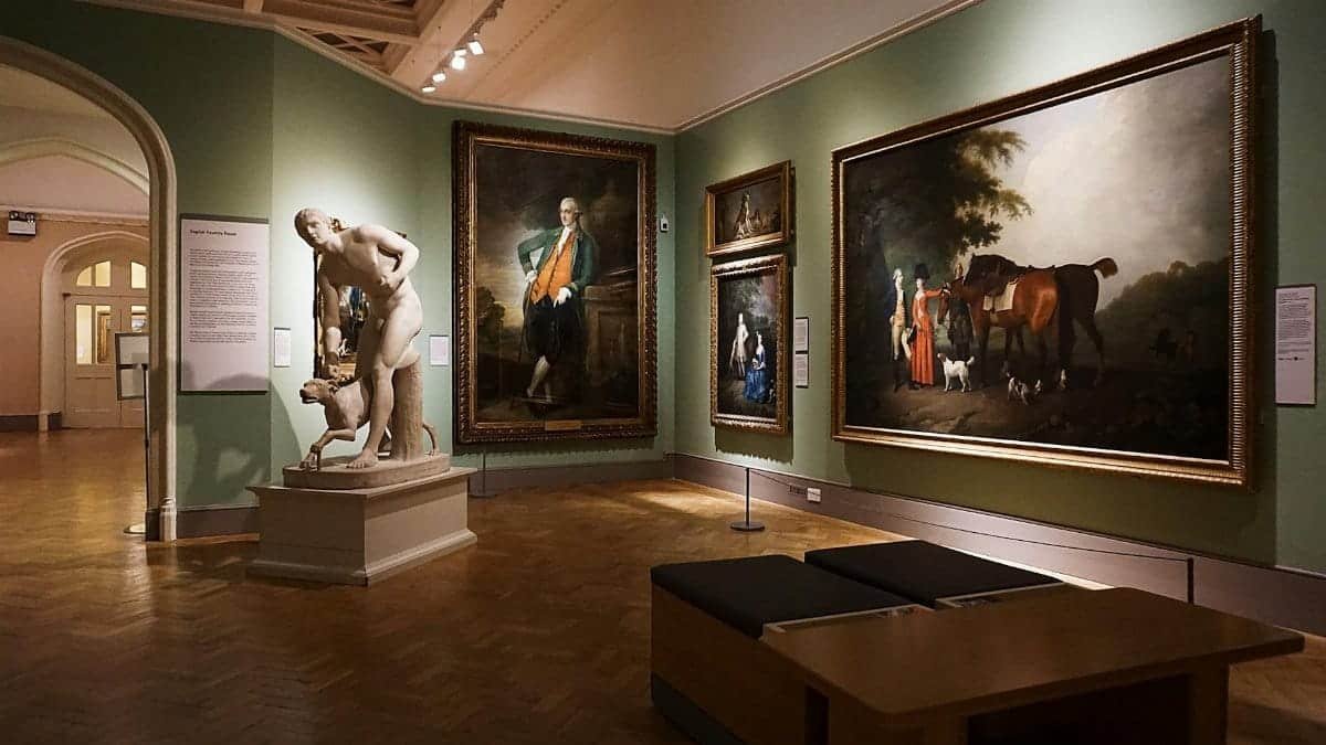 An elegant art gallery room featuring classical paintings and a prominent marble statue.