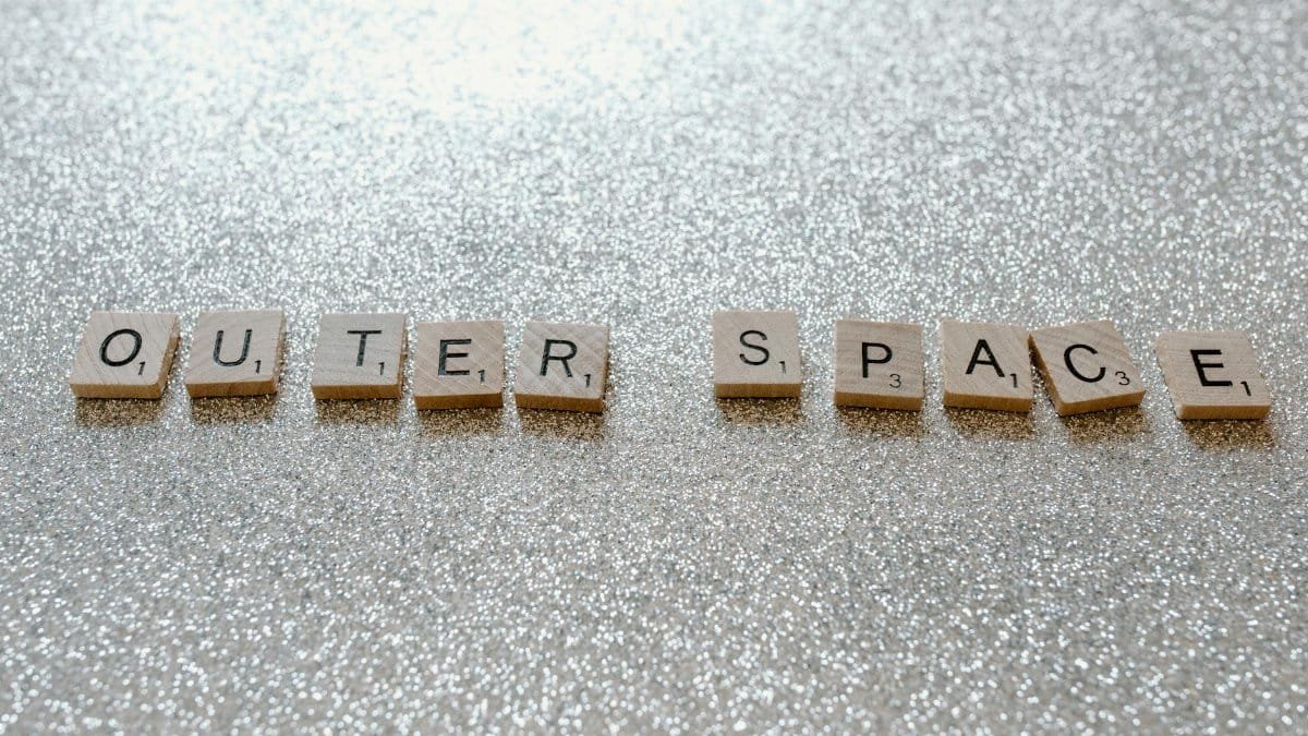 Scrabble tiles spelling 'Outer Space' on glittery surface, creative concept image.
