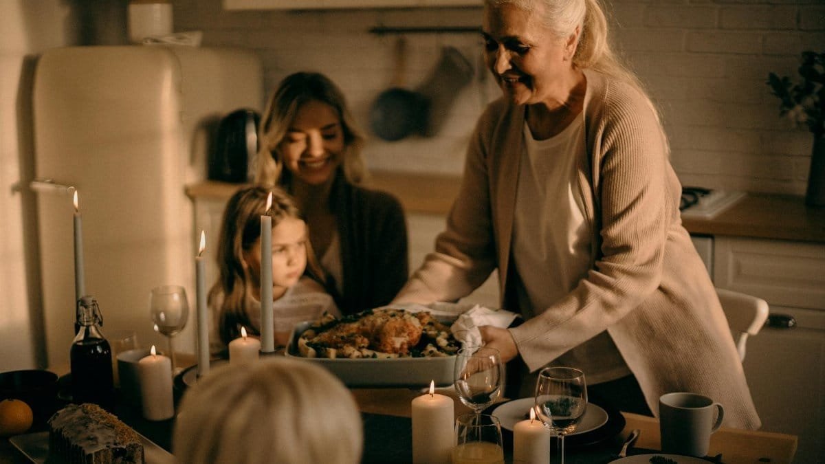 A grandmother serves a festive turkey dinner to family gathered around a warmly lit table.