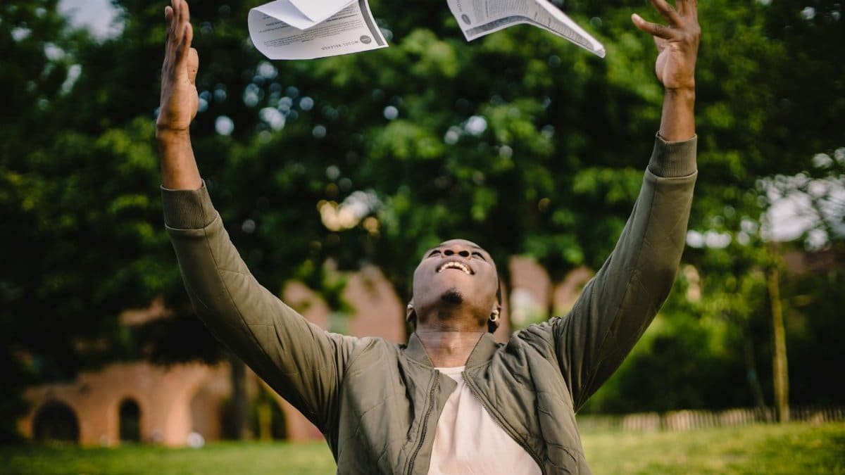 Happy African American remote worker tossing papers in air happy to get rid of boring paperwork while sitting in green park
