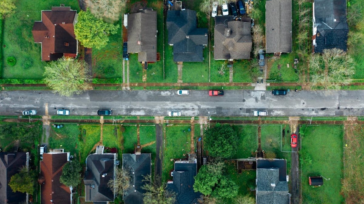 High-angle aerial shot of a suburban neighborhood street lined with houses and cars.