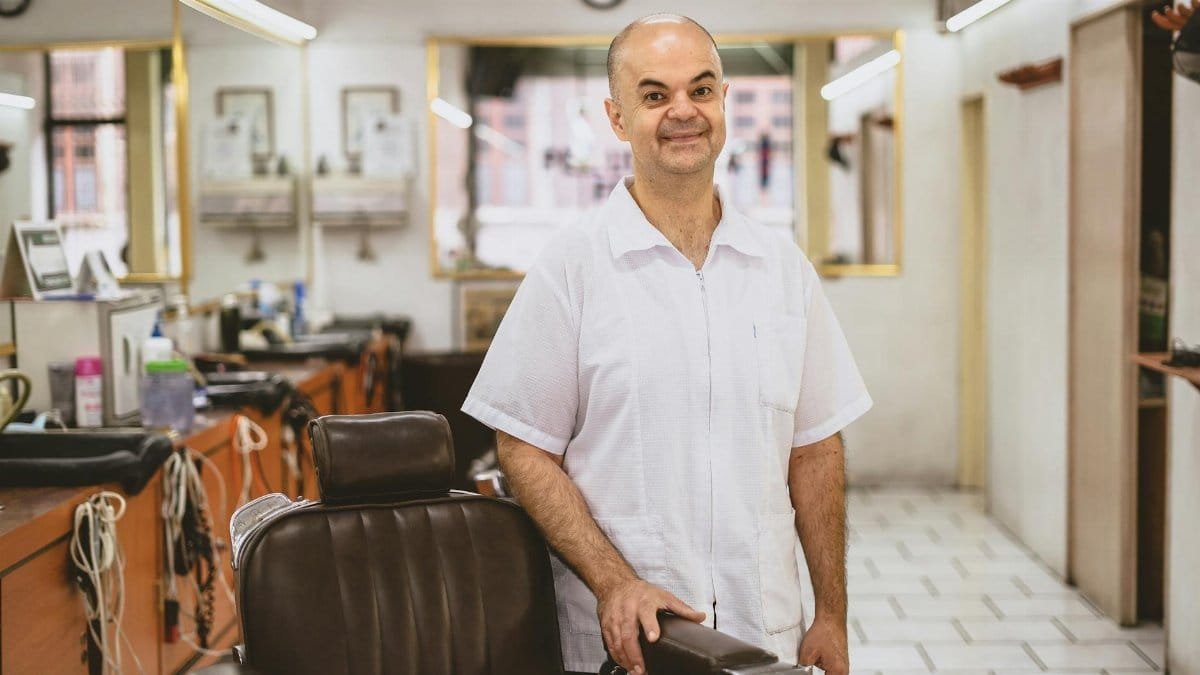 Smiling barber standing by his chair in a clean, well-equipped barbershop.