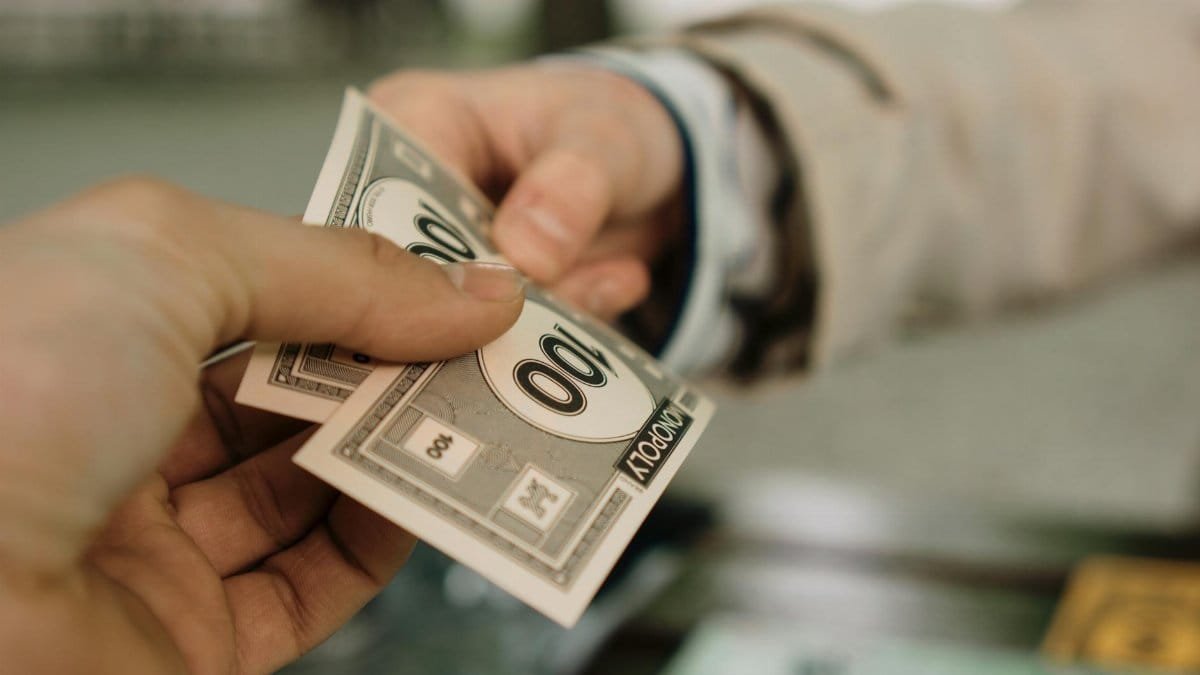 Close-up of two hands exchanging Monopoly money, symbolizing a financial transaction.