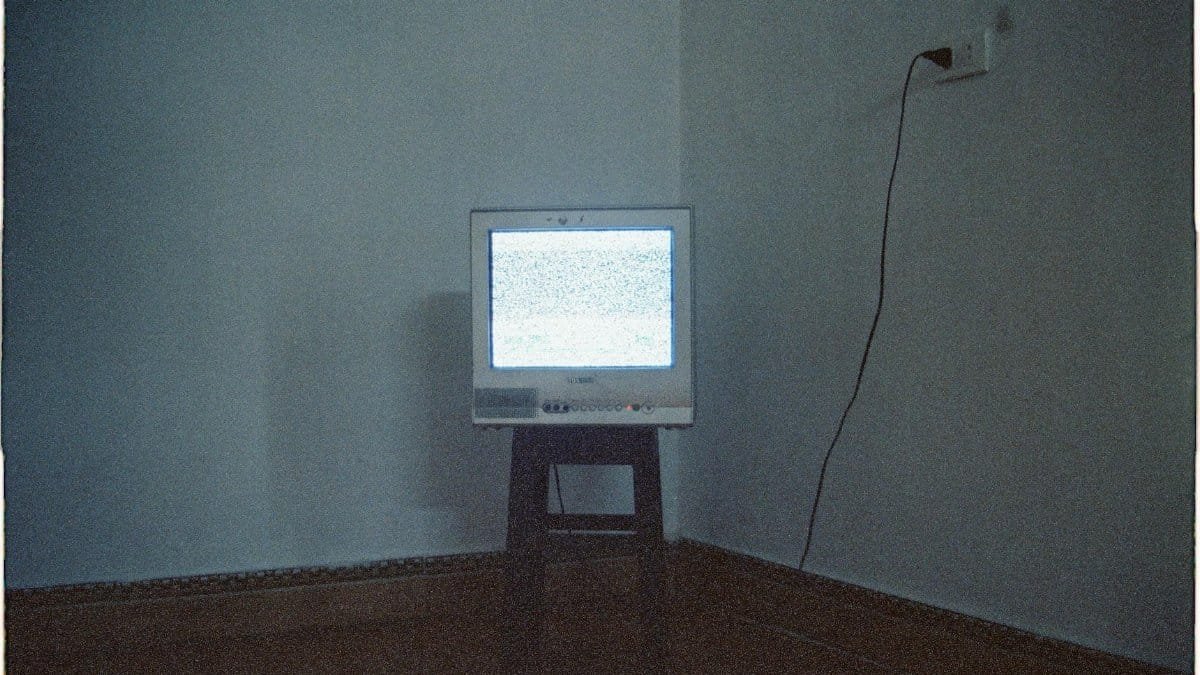 A vintage CRT television displaying static noise in a minimalist room setting.