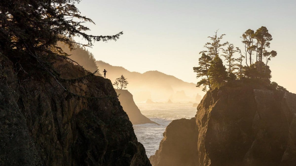 Majestic sunrise view of rugged coastal cliffs with a lone silhouette, creating a serene and dramatic seascape.
