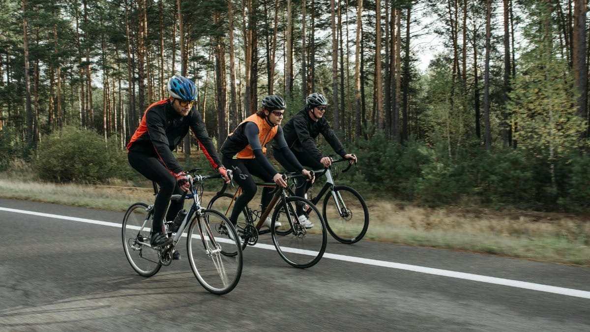 Three cyclists pedal on a forest road, engaging in outdoor sports and recreation.