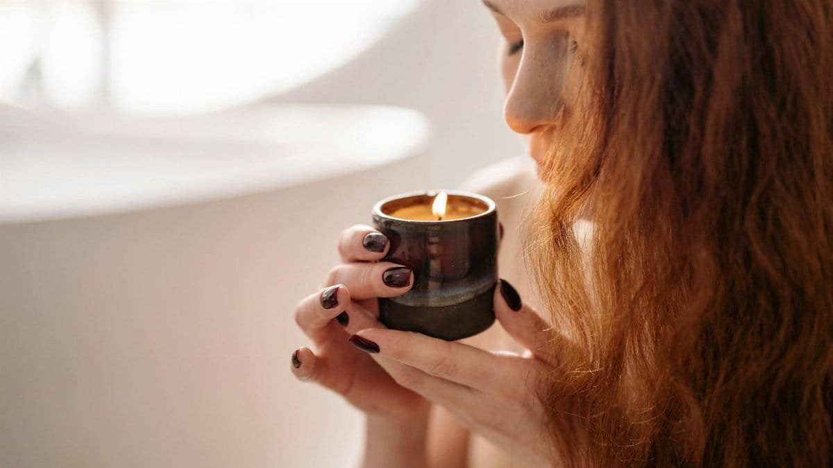 Woman enjoying the scent of a fragrant candle in a serene indoor setting.