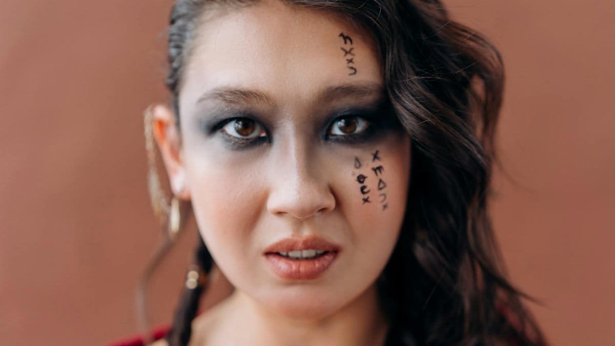 Close-up portrait of a woman with artistic makeup and mysterious symbols on her face.