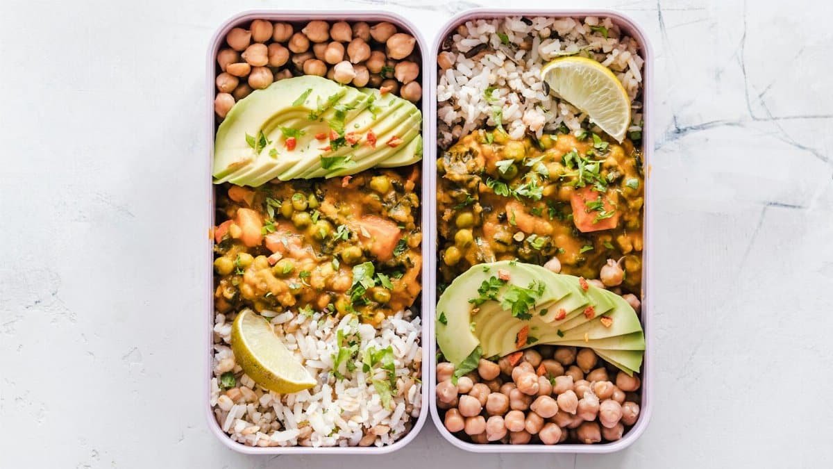 Delicious vegan lunchboxes featuring chickpeas, rice, avocado, and curry on a white background.
