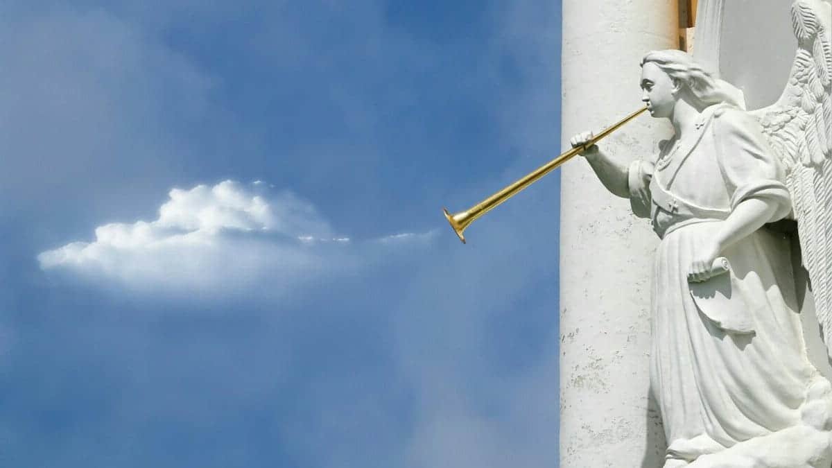 Sculpture of an angel with a trumpet, set against a bright blue sky with clouds.