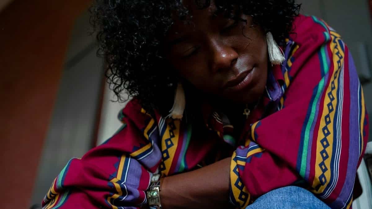 A close-up portrait of a person with curly hair wearing a colorful striped shirt indoors.
