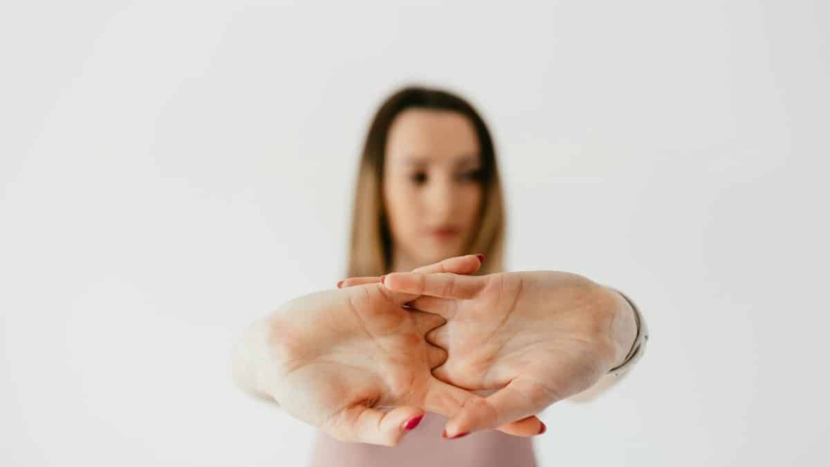 Blurred content fit lady in casual wear stretching arms while standing against gray wall and looking away