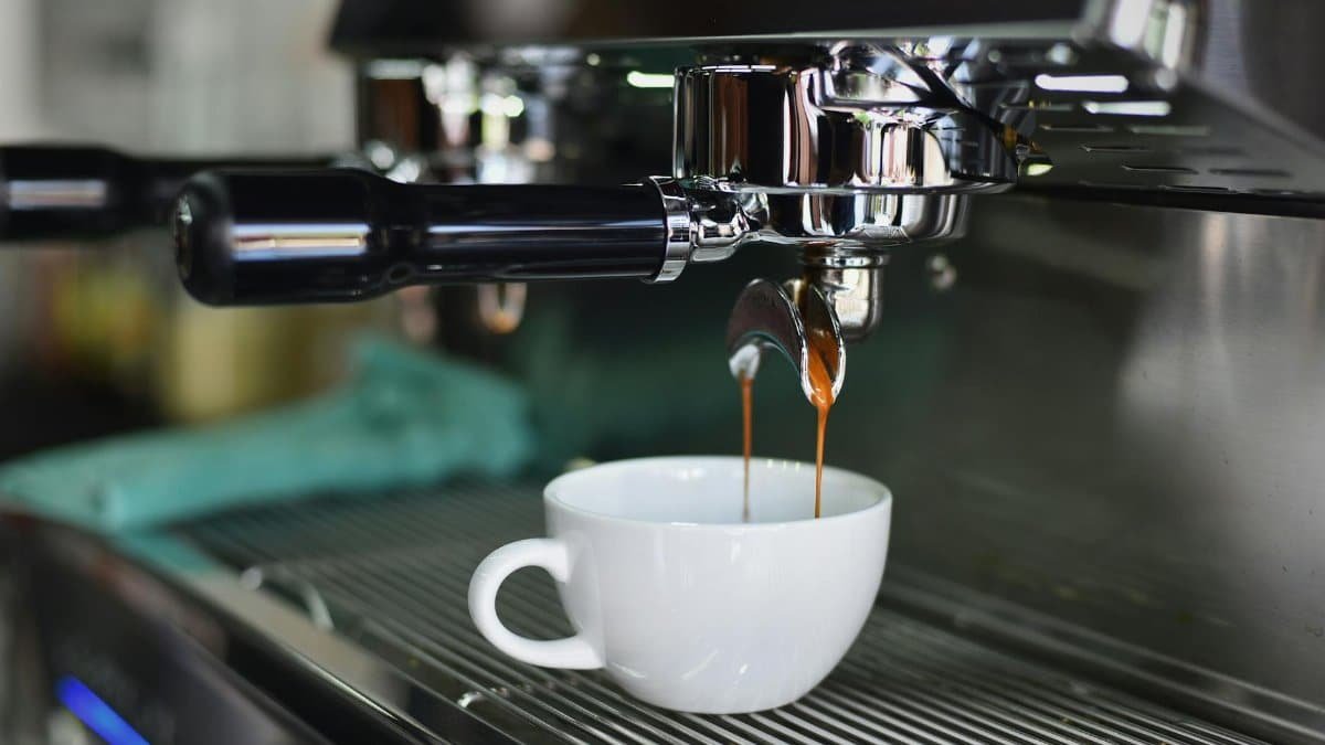 Close-up of espresso pouring from a shiny coffee machine into a white cup, perfect for lovers of caffeine and barista art.
