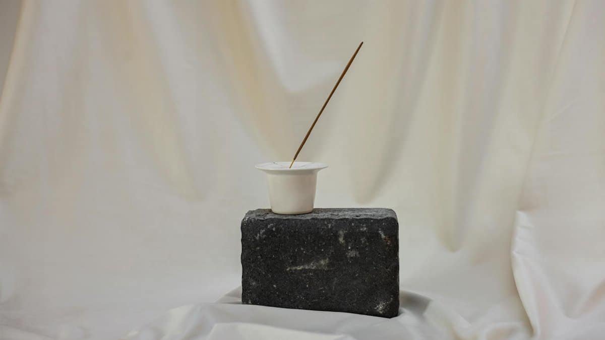 Simple arrangement of a cup and stick on a stone against a white curtain backdrop.