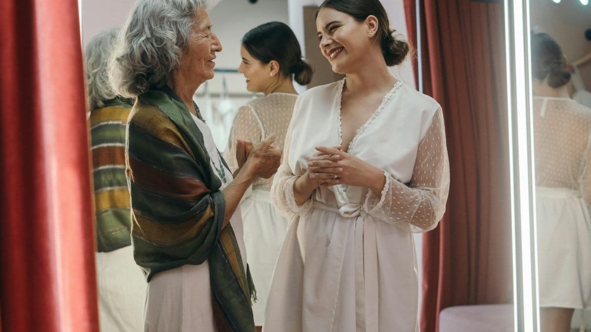 Two women, one elderly and one adult, share a joyful moment in front of a mirror indoors.