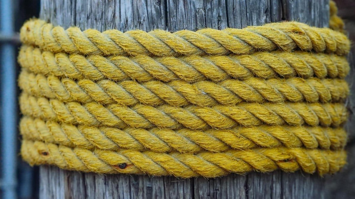 Detailed view of a thick yellow jute rope coiled around a rustic wooden post.