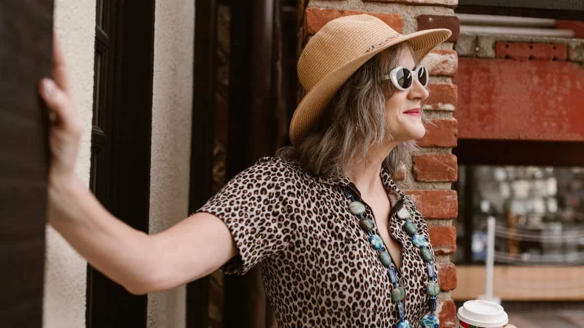 A fashionable senior woman in leopard print and sunglasses holding coffee in a vibrant city setting.