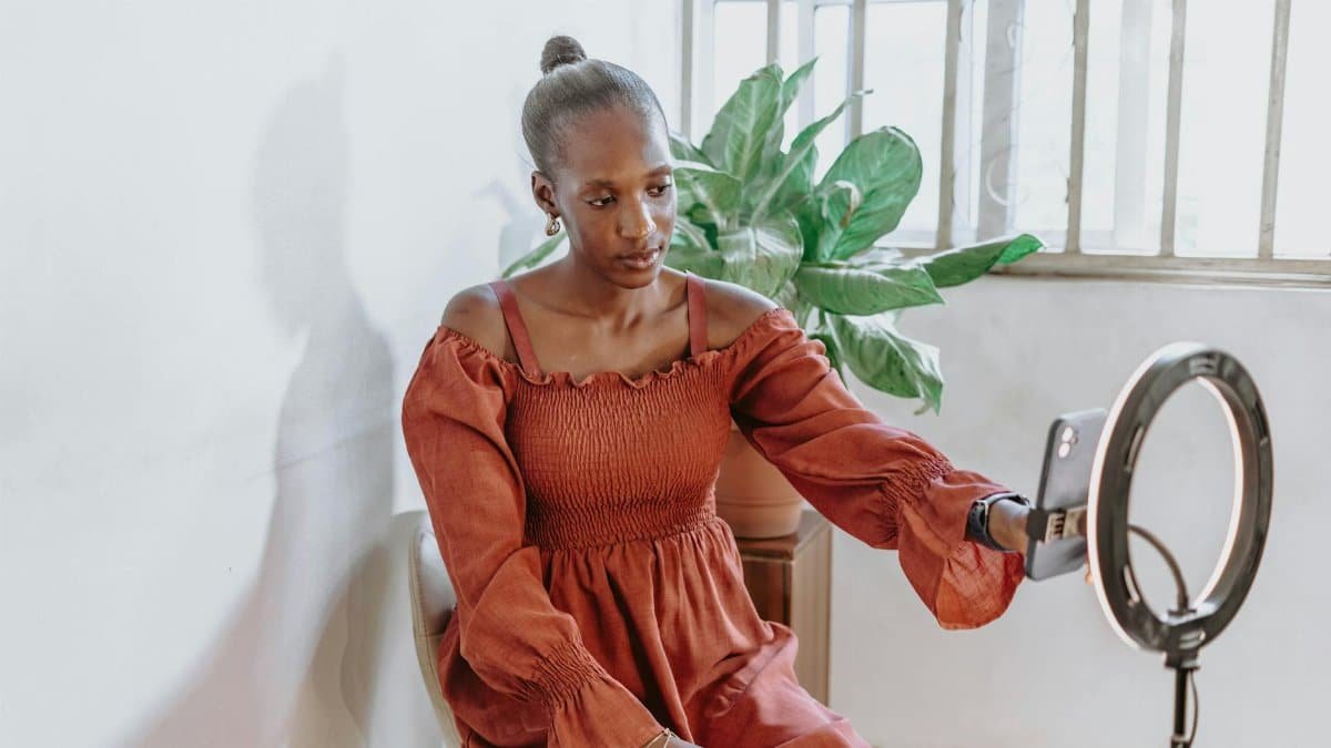 Fashionable woman vlogging indoors with ring light and phone in Abuja, Nigeria.