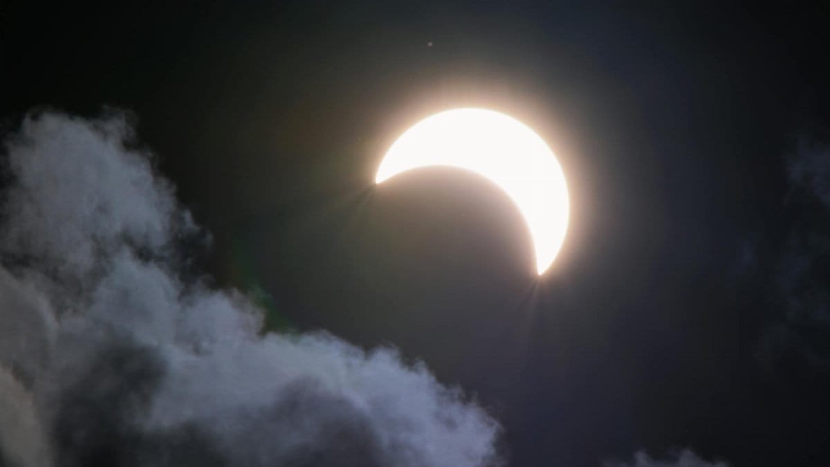 A bright crescent moon partially hidden by clouds at night, creating a dramatic celestial scene.