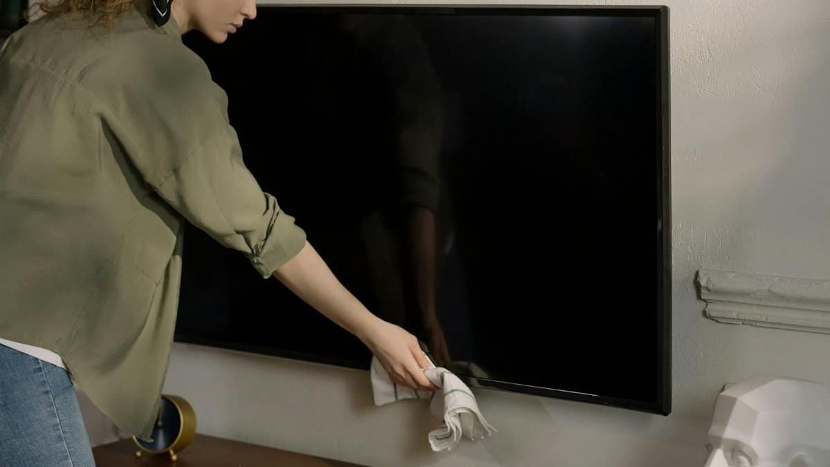 A woman cleaning a black screen TV in a cozy home environment, promoting cleanliness.
