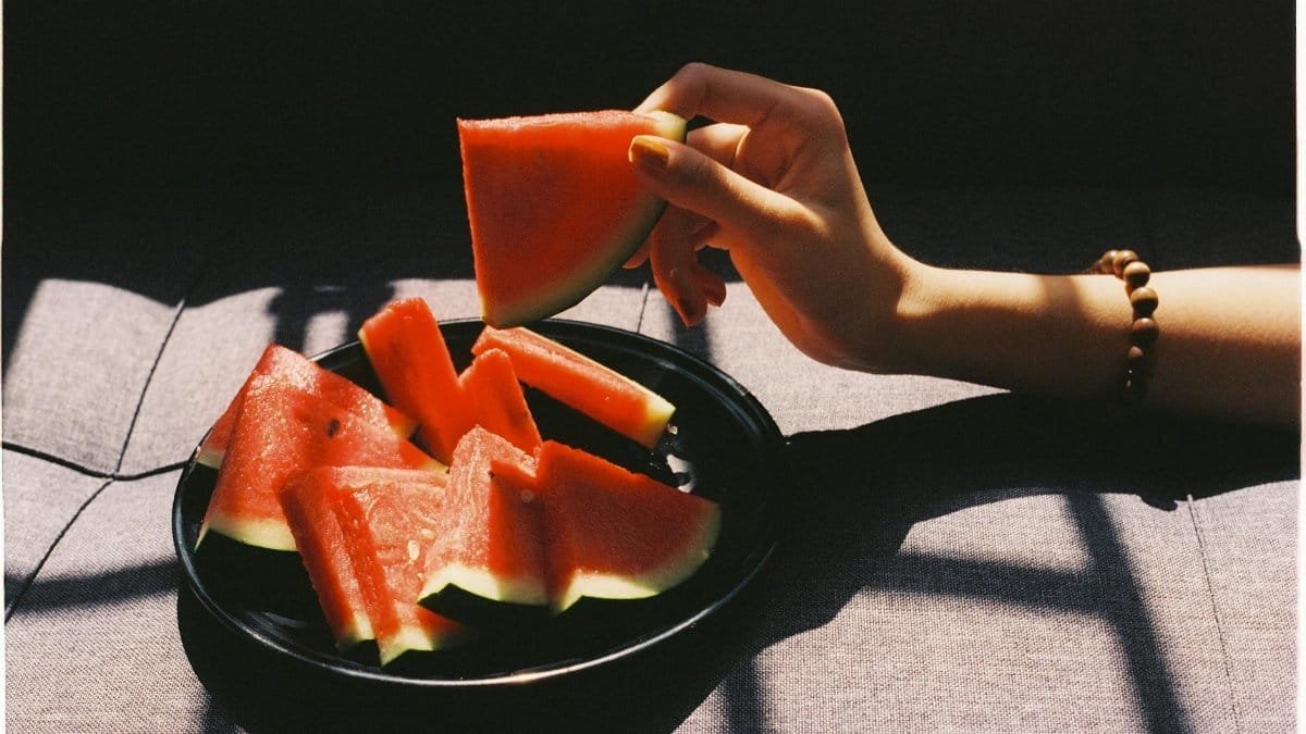 A hand picking a slice of watermelon in natural light.