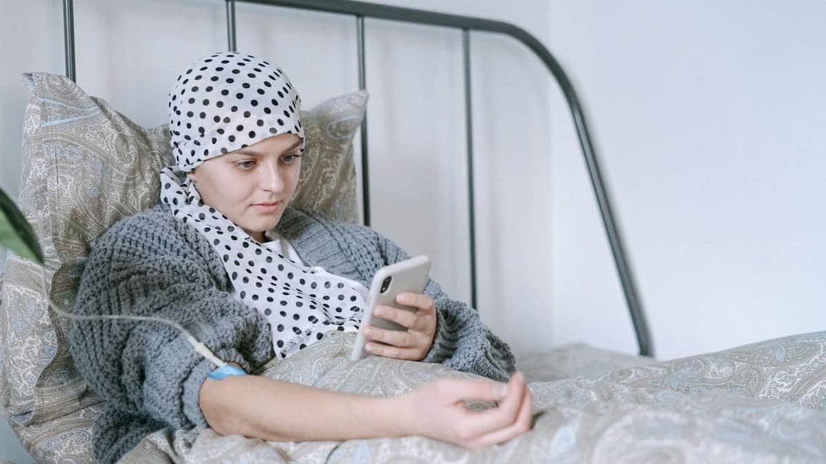 Woman in bed undergoing cancer treatment, looking at her phone with hope and determination.