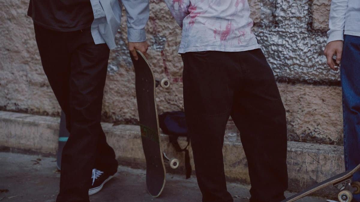Three skaters stand outdoors holding skateboards, ready for action. Casual urban vibe.